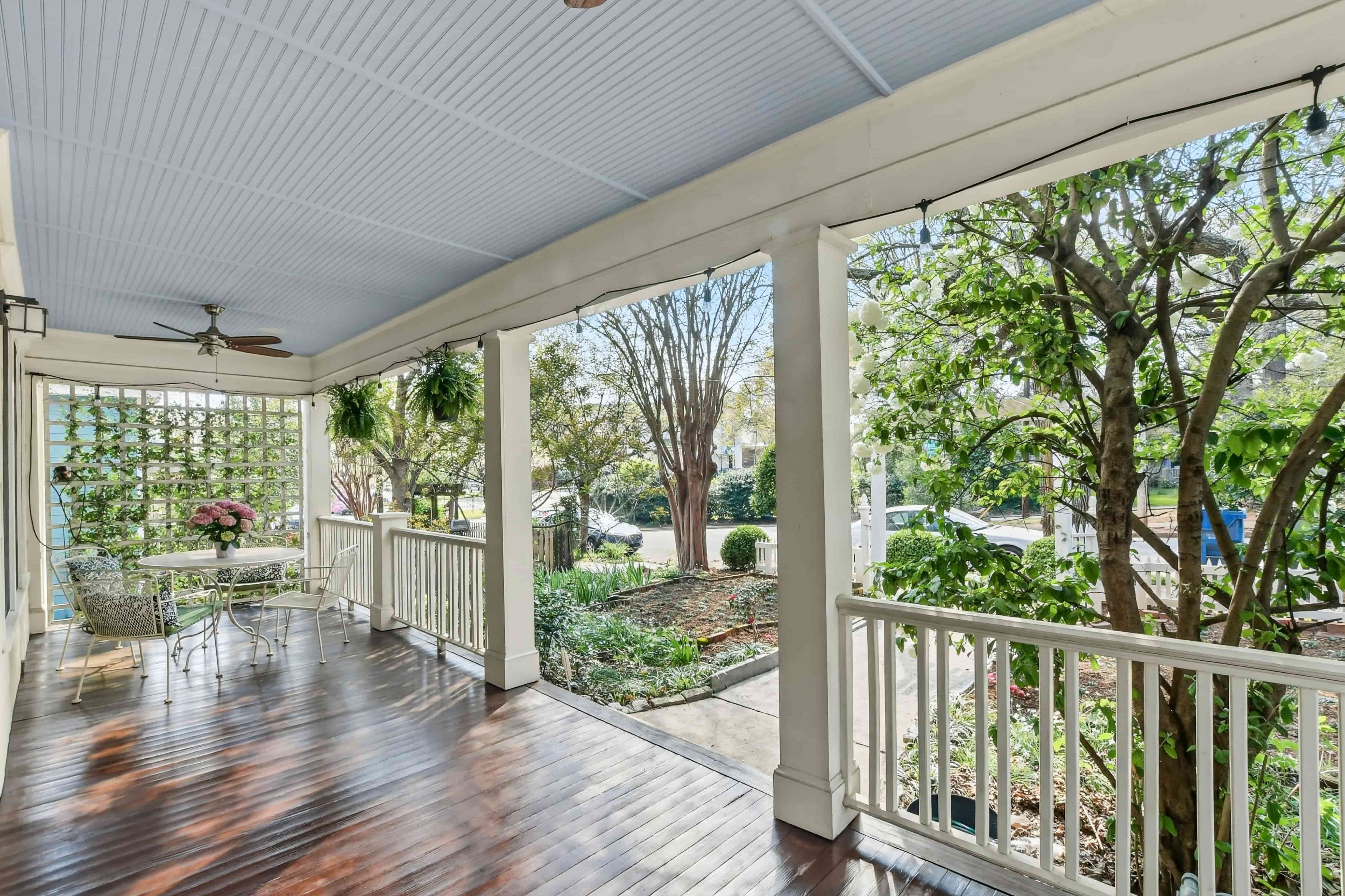 Covered front porch with hardwood floor, bistro seating, ceiling fan, and a view of the front garden